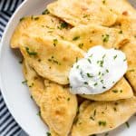 A plate of Potato and Cheese Pierogis with sour cream and topped with freshly chopped chives