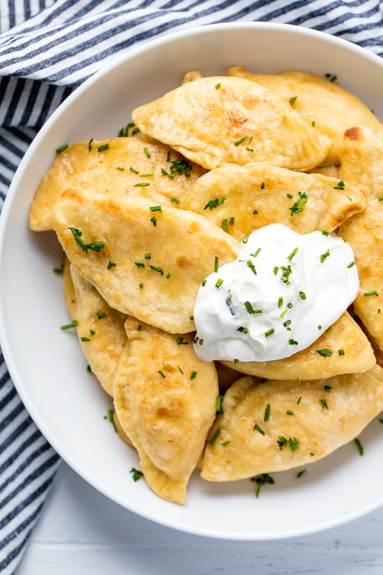 A plate of Potato and Cheese Pierogis with sour cream and topped with freshly chopped chives