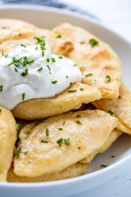 A plate of Potato and Cheese Pierogis with sour cream and topped with freshly chopped chives