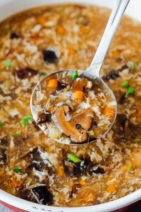 A ladle of Chicken Hot and Sour Soup with mushroom, carrot, celery and tofu taken from a pot