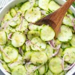 Cucumber Salad in a white bowl with a wooden spoon in it.