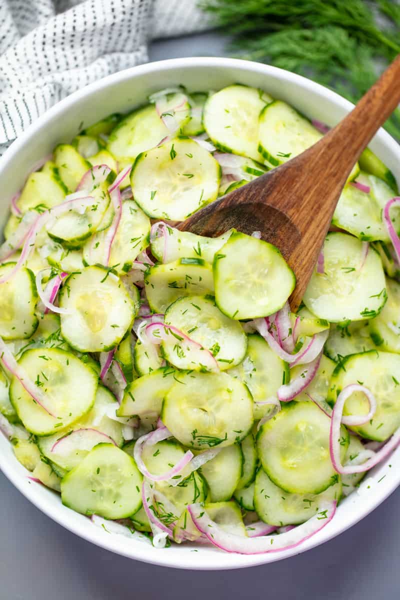 Cucumber Salad in a white bowl with a wooden spoon in it.