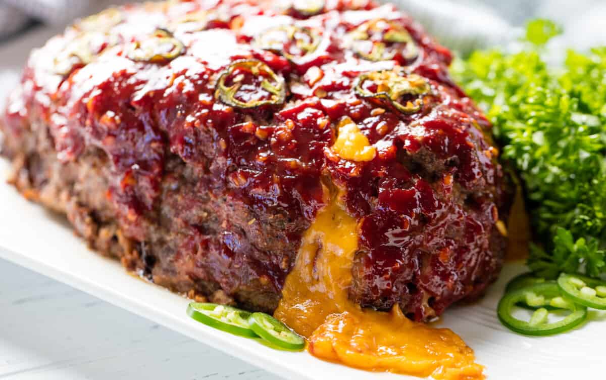 Jalapeno cheddar stuffed meatloaf with cheese oozing out on a white plate