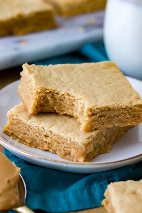 Peanut Butter Blondies stacked on a plate. One with a bite taken out of it