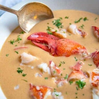 Lobster Bisque in a white bowl with a brass spoon in it.