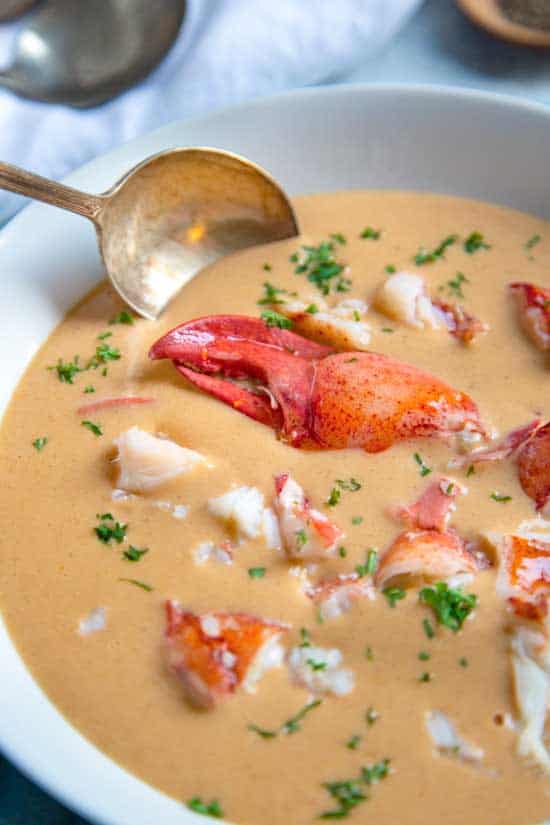 Lobster Bisque in a white bowl with a brass spoon in it.