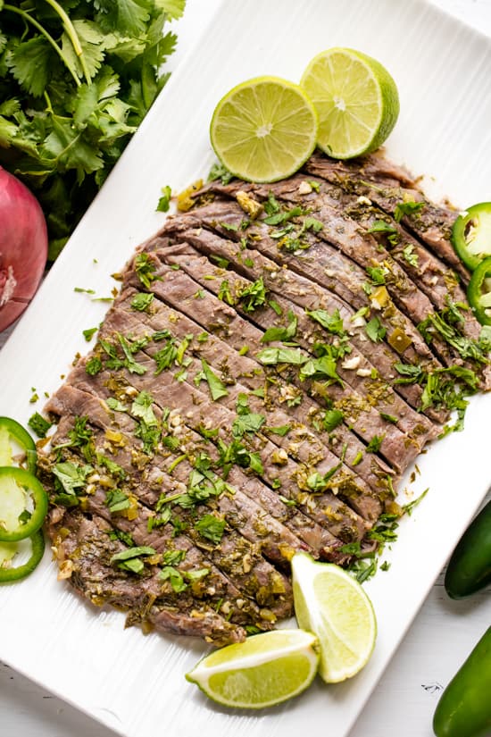 Slow Cooker Carne Asada sliced and served on a platter with cilantro, lime wedges and slices of jalapeno