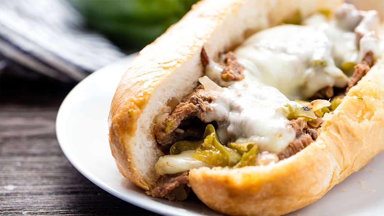 Angled view of Philly Cheese Steak with green bell peppers and melted Kraft provolone cheese on a hoagie roll.