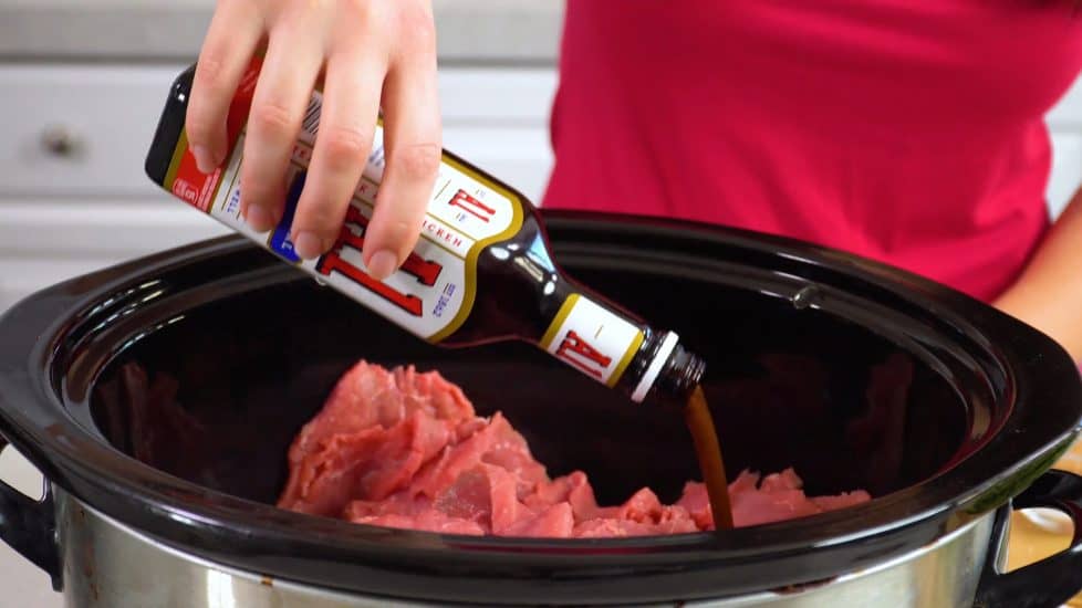 Rachel pours A-1 sauce over round beef roast in a slow cooker