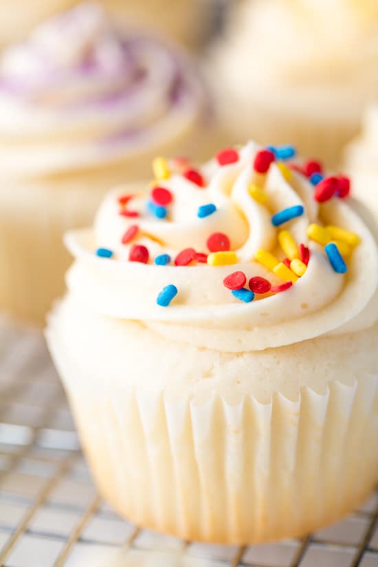 White cupcake topped with a buttercream frosting and colorful sprinkles.
