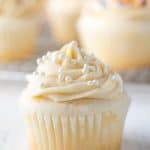 White cupcake topped with a buttercream frosting and white sprinkles.