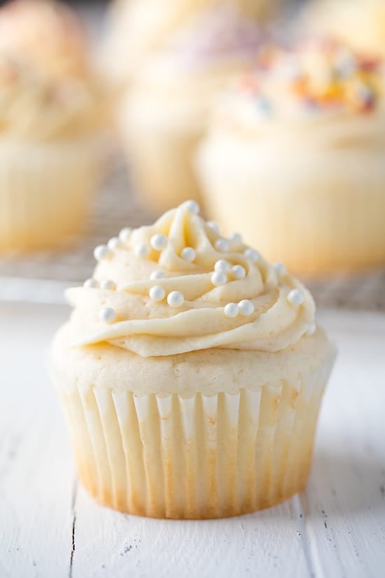 White cupcake topped with a buttercream frosting and white sprinkles.