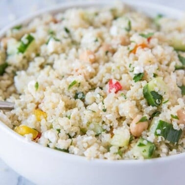 Quinoa salad in a white bowl with a metal spoon in it.
