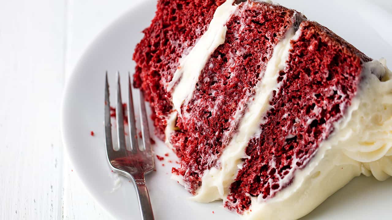 Slice of red velvet cake on a white plate with a fork and bite taken out