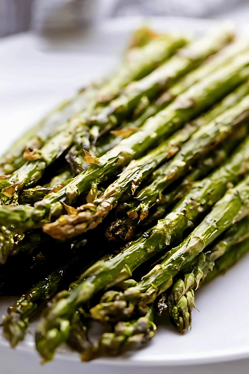 A closeup view of a pile of roasted asparagus on a white plate.