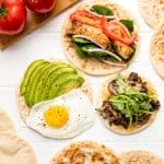 Bird's eye view of 3 flatbread recipes, an avocado and egg flatbread, a muhsroomm and arugula flatbread, and spinach, onion, grilled chicken, and tomato flatbread.