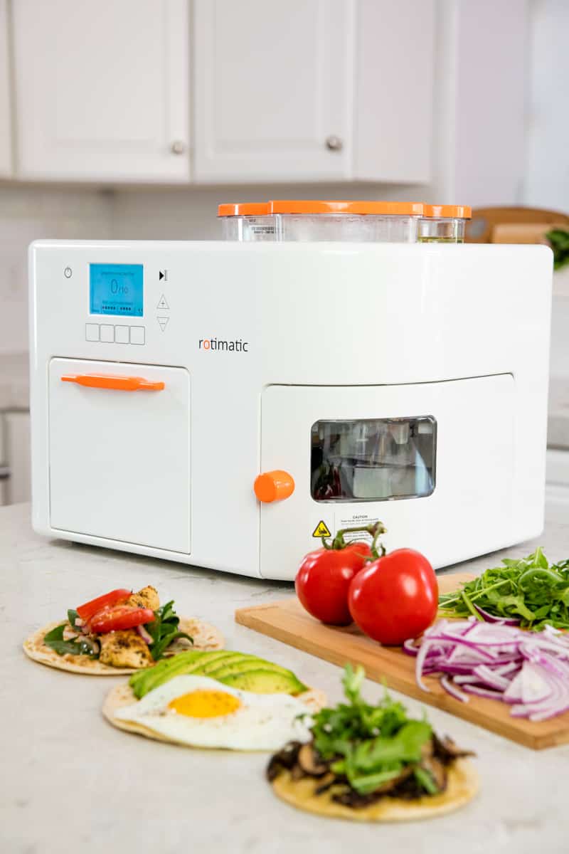 Rotimatic sitting on a countertop with some completed flatbread recipes and ingredients. 