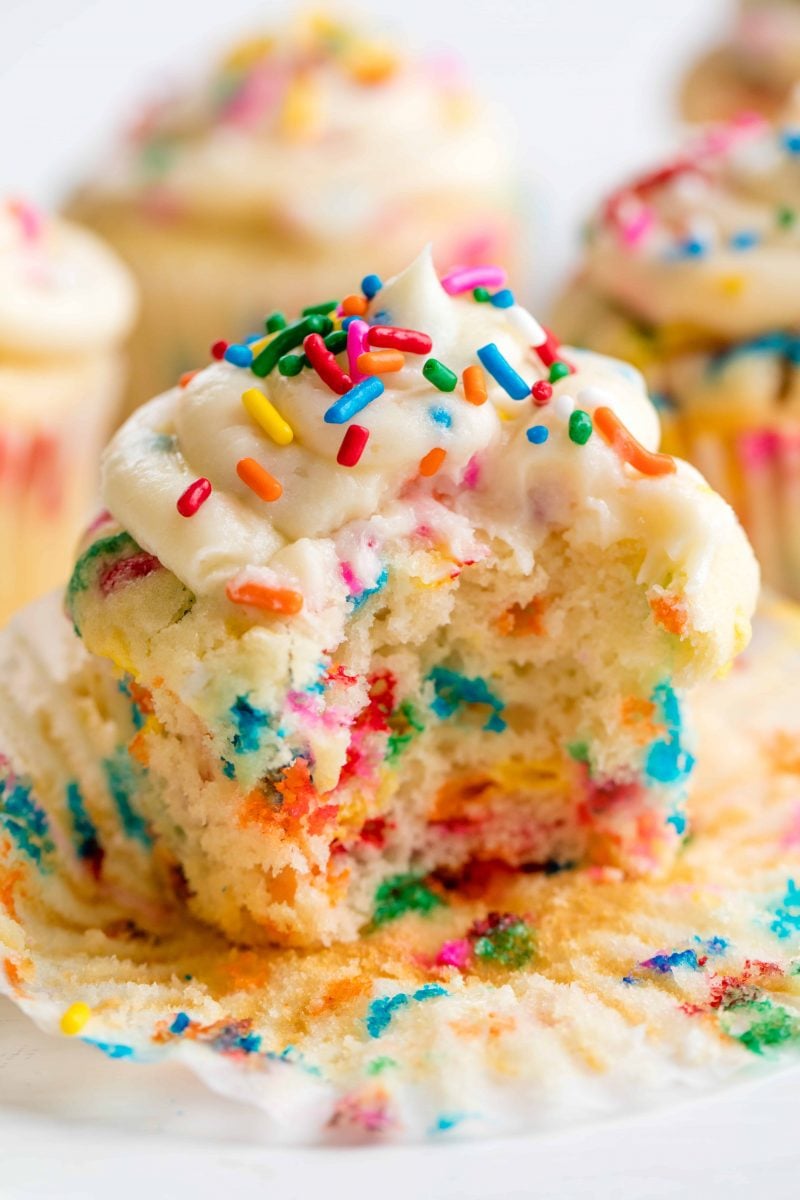 Close up of a funfetti birthday cupcake with the wrapper undone and a bite taken out of it. 