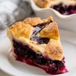 Slice of blueberry pie sitting on a white plate.