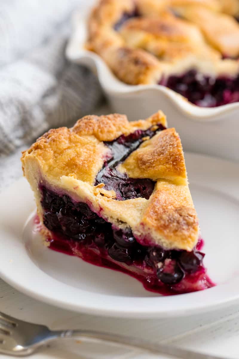 Slice of blueberry pie sitting on a white plate. 