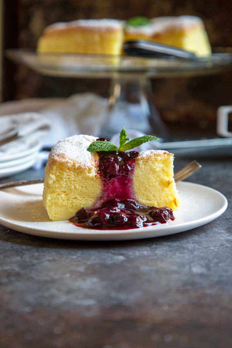 Japanese Cheesecake on a white plate topped with powdered sugar, a berry topping, and a mint leaf.