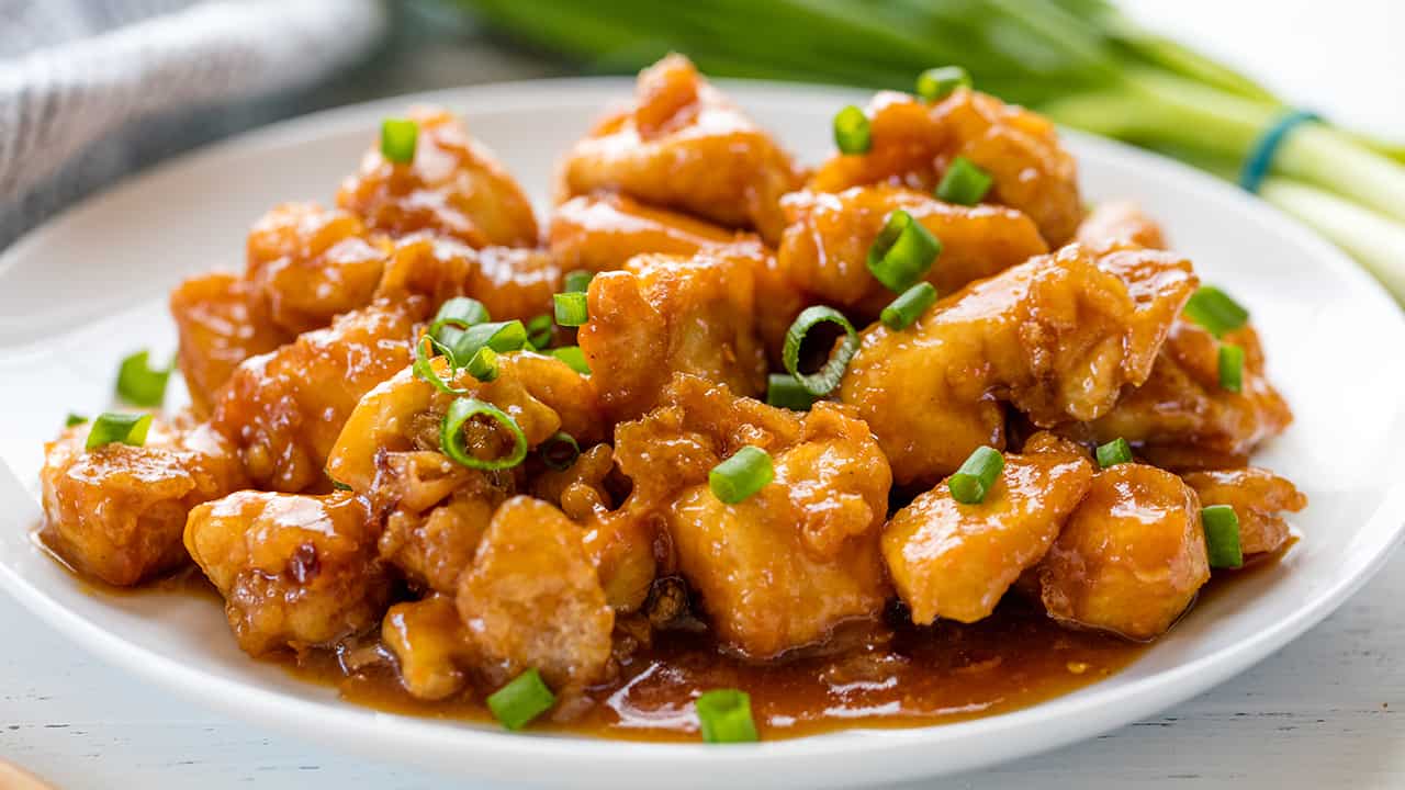 Orange chicken topped with green onions on a white plate.