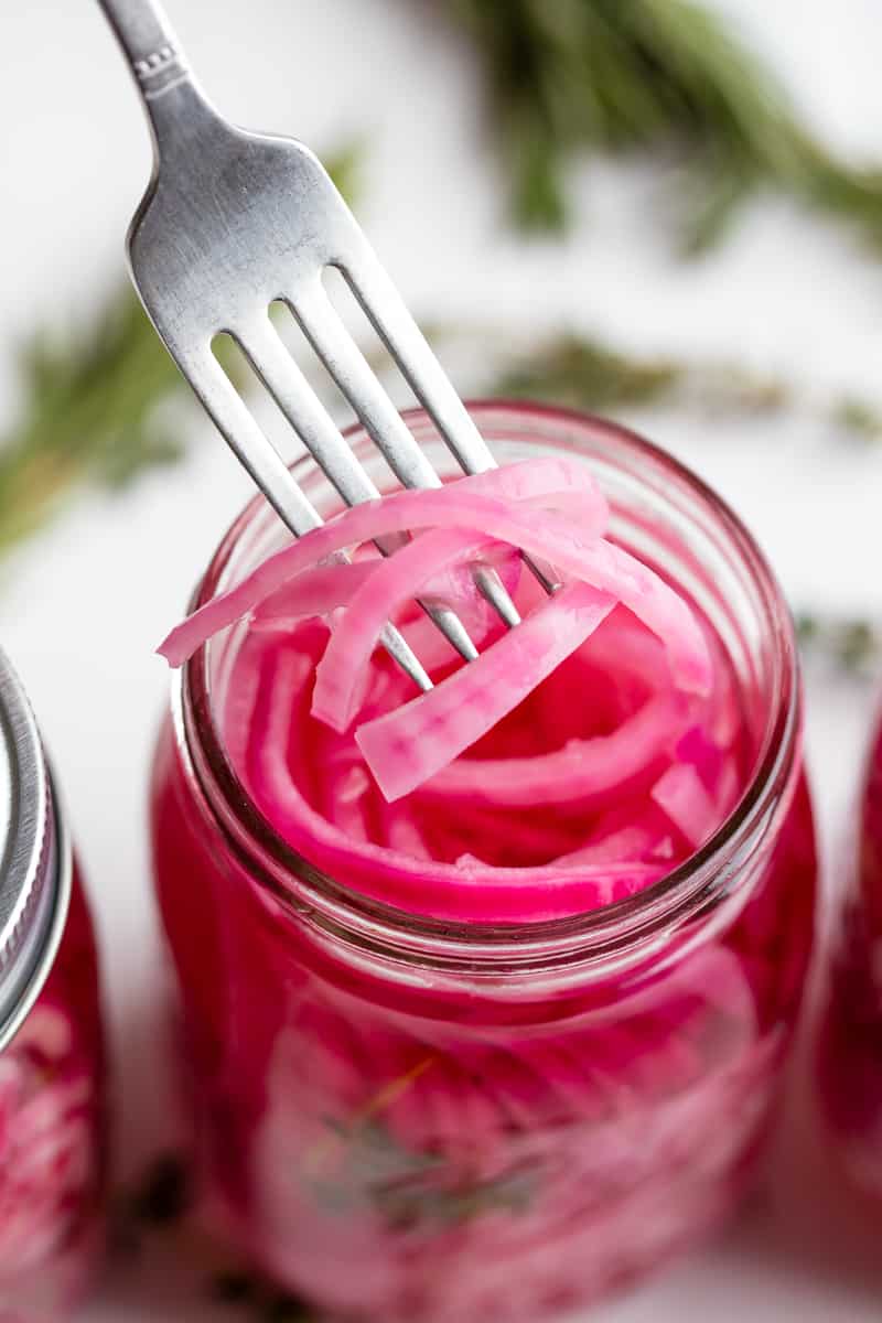 Fork pulling out some pickled red onions from a mason jar.