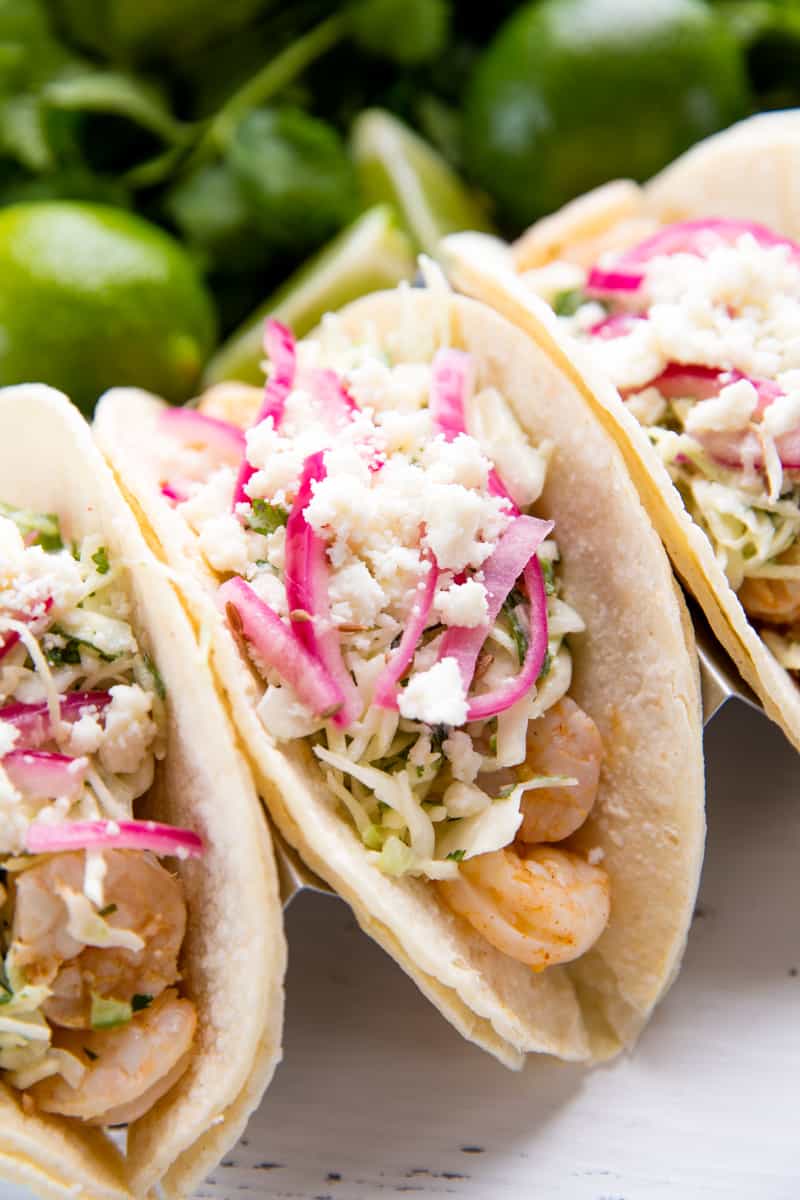 Close up of a shrimp taco topped with coleslaw, onions, and feta cheese.