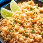 Spanish Rice with two lime wedges in it in a dark bowl.