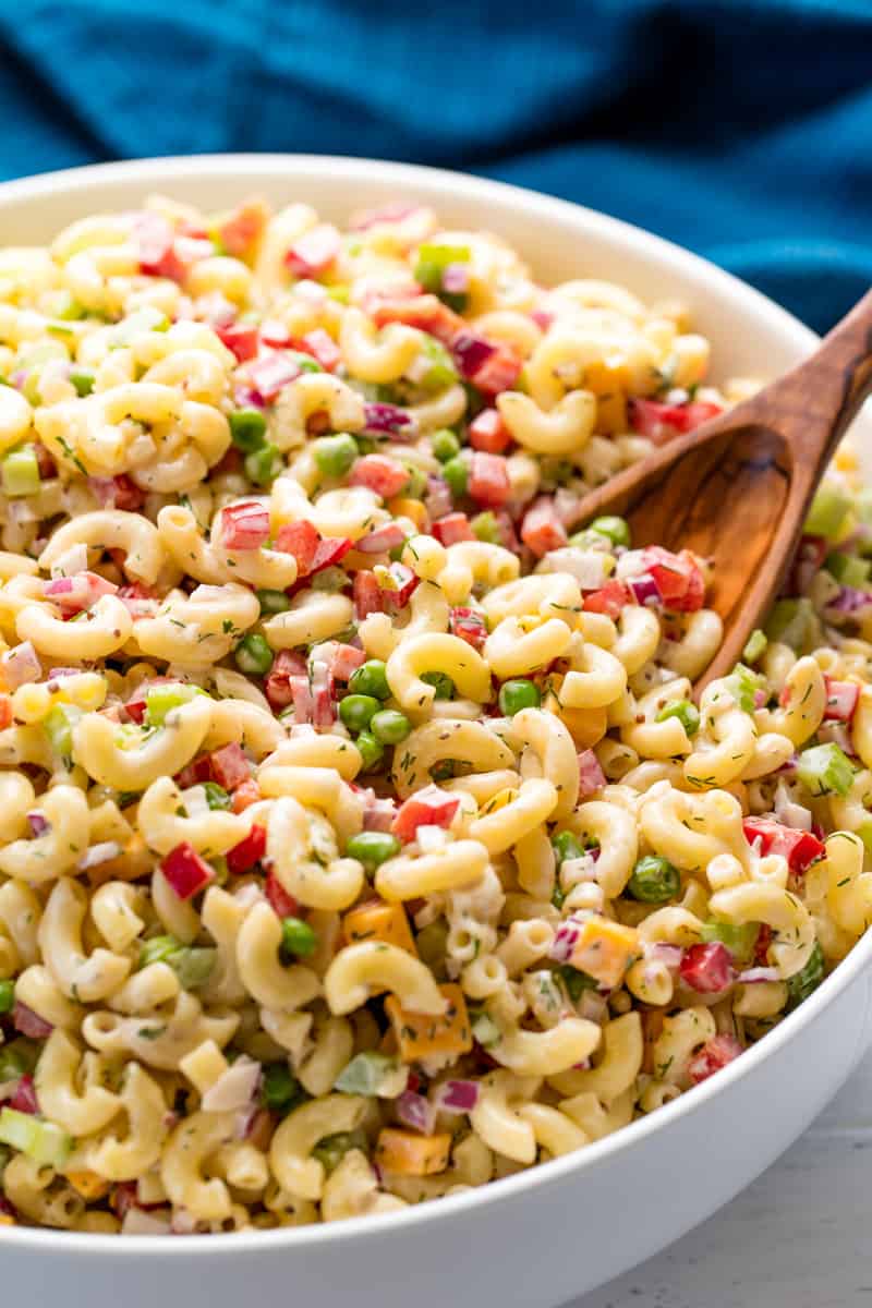 Close up of bowl full of macaroni salad with a wooden spoon in it.