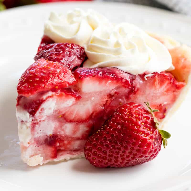 A slice of Strawberry Pie on a white plate with a strawberry by it.