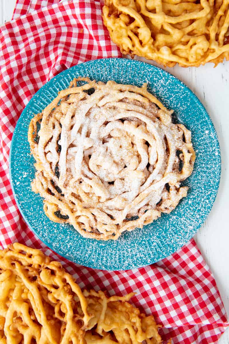 A funnel cake sprinkled with powdered sugar on a blue plate