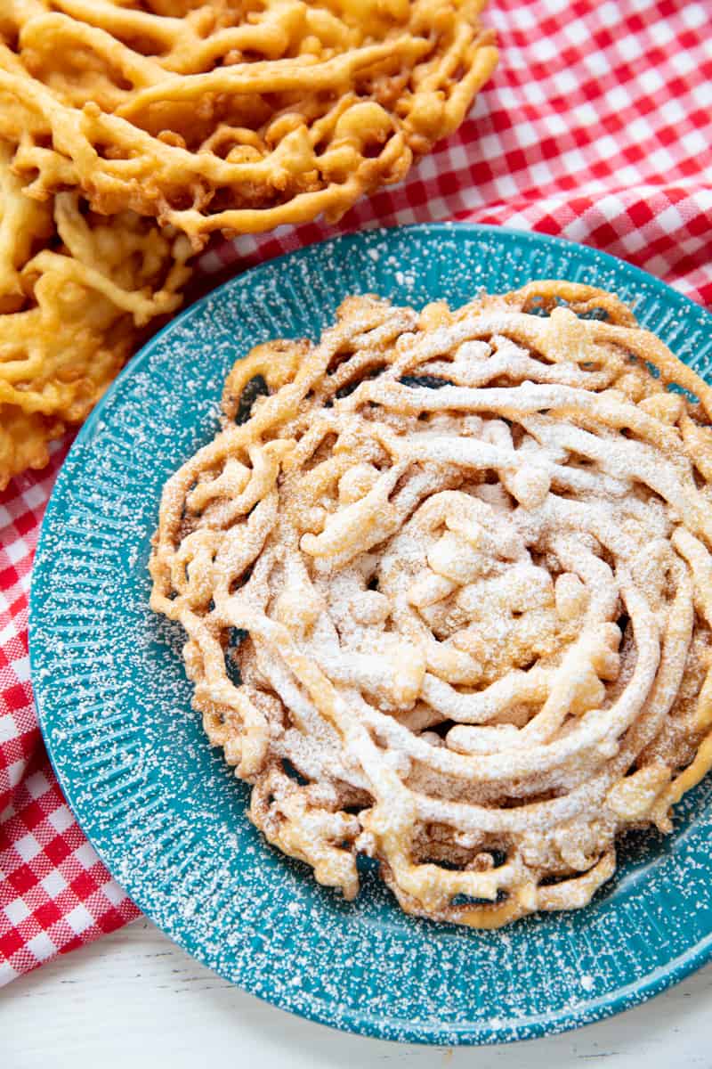 A funnel cake sprinkled with powdered sugar on a blue plate