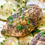 A baked chicken breast seasoned with lemon pepper and chopped fresh parley, surrounded by sliced lemon