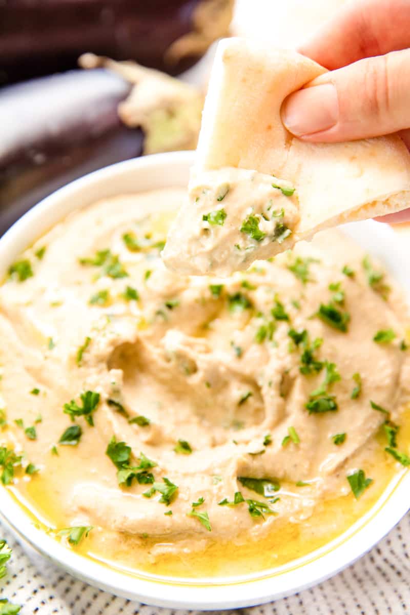 A piece of pita bread being dipped into a bowl of Baba Ganoush