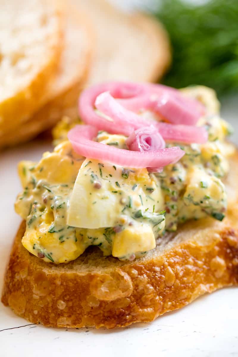 Egg Salad served up on a slice of bread topped with pickled onions. 