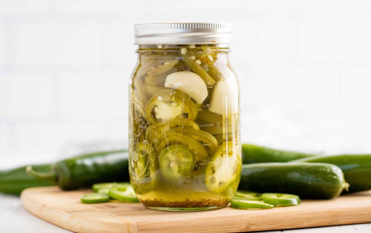 Pickled jalapenos on a cutting board surrounded by jalapenos.