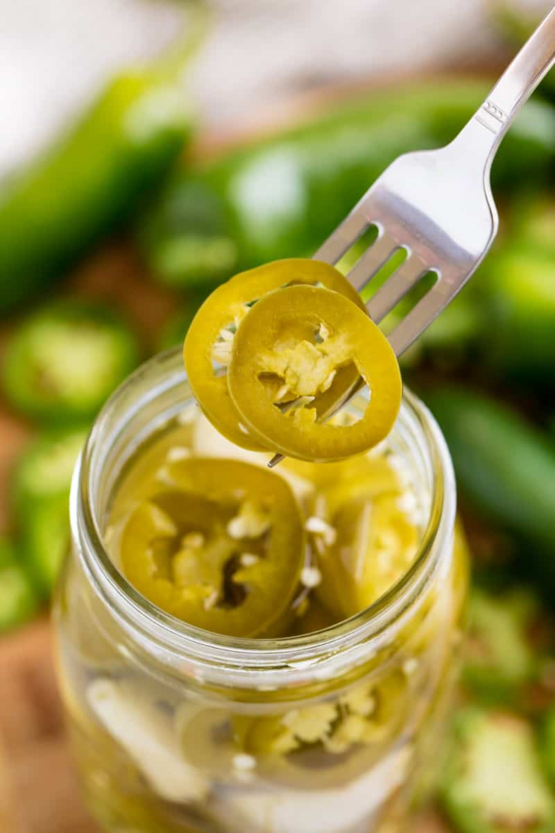  A fork lifts a couple pickled jalapenos from a mason jar