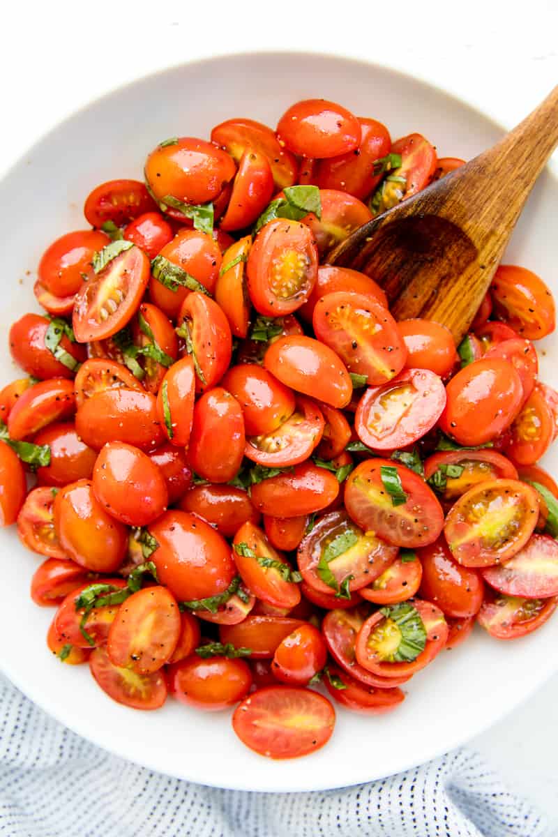 Balsamic Tomato Salad in a white bowl with a wooden spoon