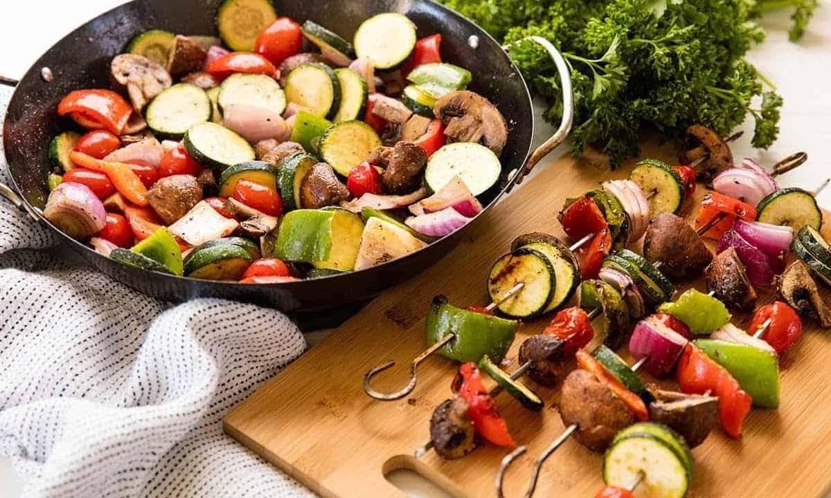 Grilled vegetables in a skillet and on skewers.