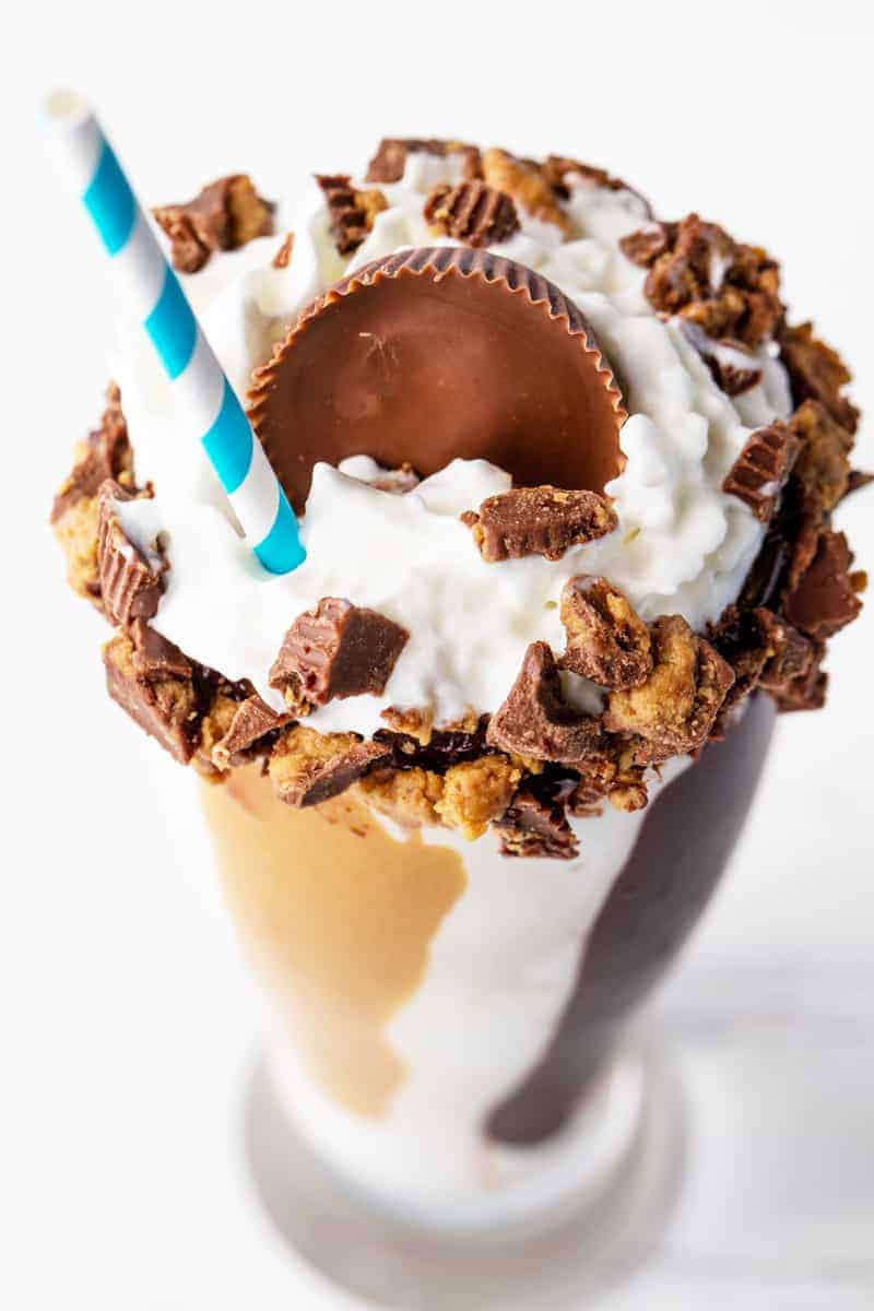 Bird's eye view of a Chocolate Peanut Butter Milkshake in a tall glass with a straw topped with crumbles up Reese's peanut butter cups, whipped cream, and full Reese's peanut butter cup on top.