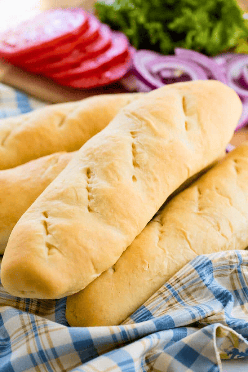 A pile of homemade hoagie rolls with sandwich ingredients in the background.