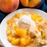 Served up peach cobbler on a white plate topped with a scoop of ice cream.