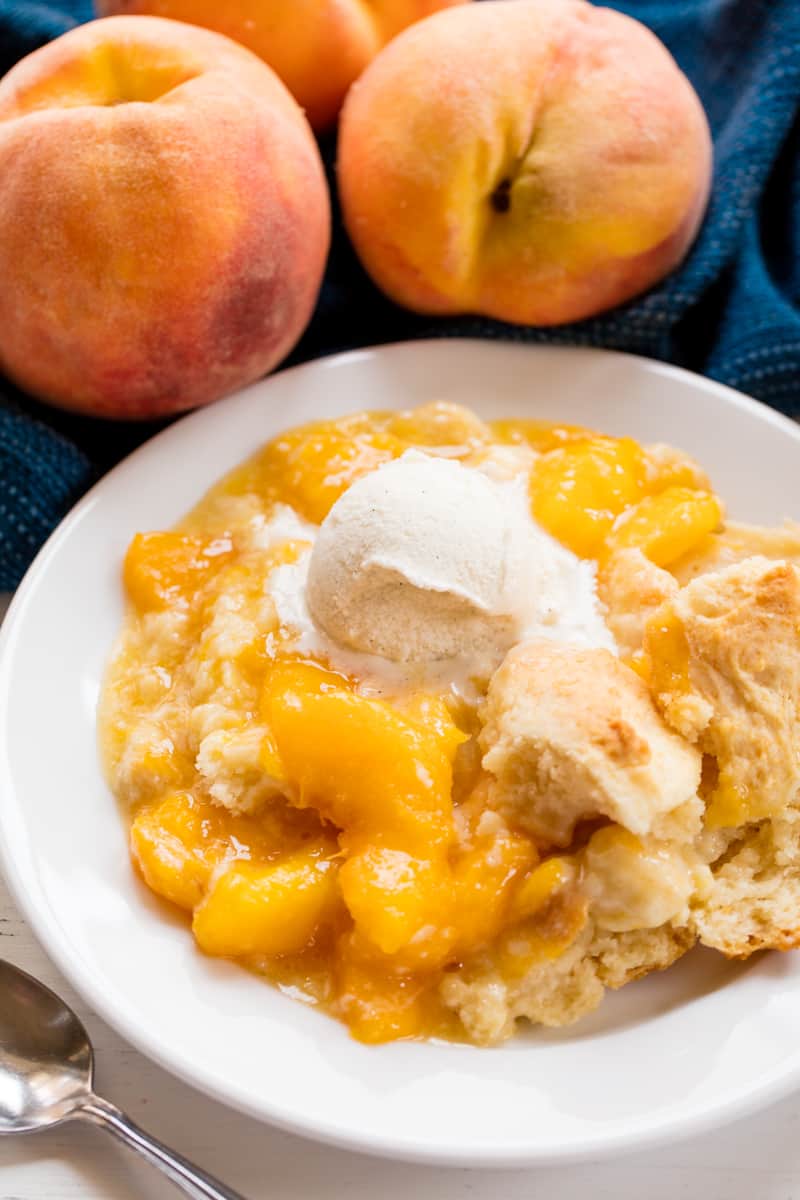 Served up peach cobbler on a white plate topped with a scoop of ice cream.