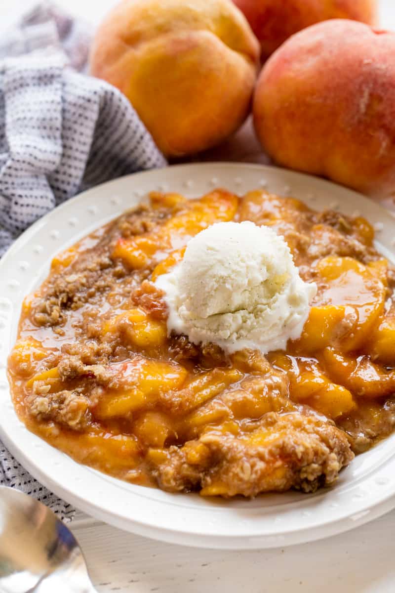 Peach Crisp served up on a white plate with a scoop of vinalla Icecream in the center.