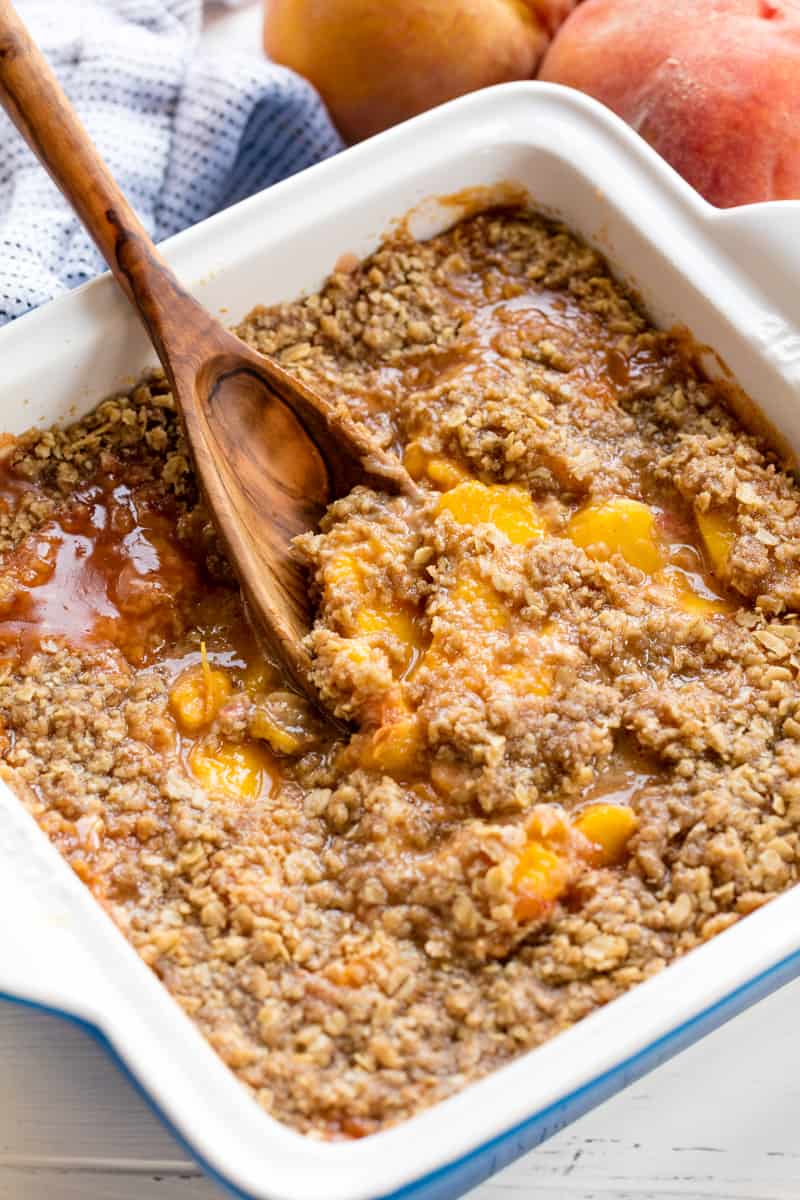 Peach Crisp in a 9 x 9 pan getting scooped up by a wooden spoon. 