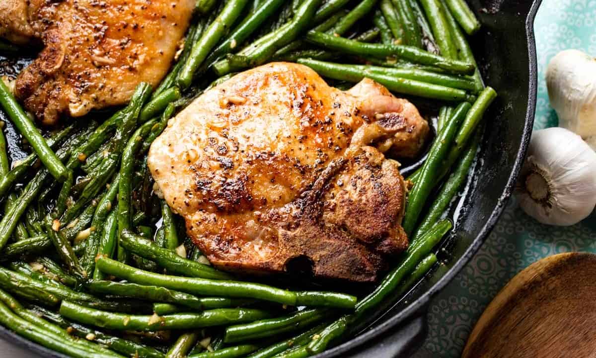 Pork chop in a skillet surrounded by green beans