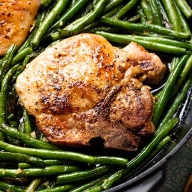 Pork chop in a skillet surrounded by green beans
