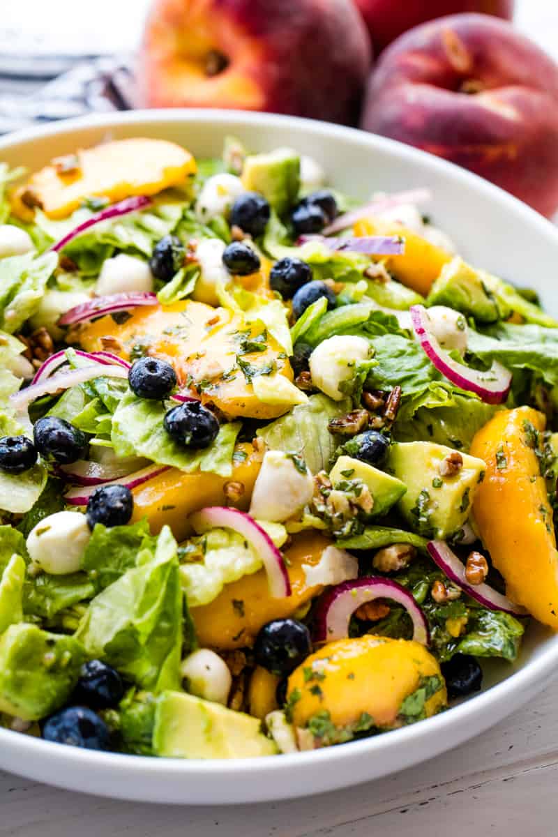 Variety of summer salads on a table, including summer pasta salad, summer fruit salad, and a leafy green summer salad with fresh strawberries.