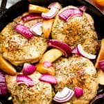 A skillet full of Apple Stuffed Pork Chops slightly covered by onion slices and apple wedges.